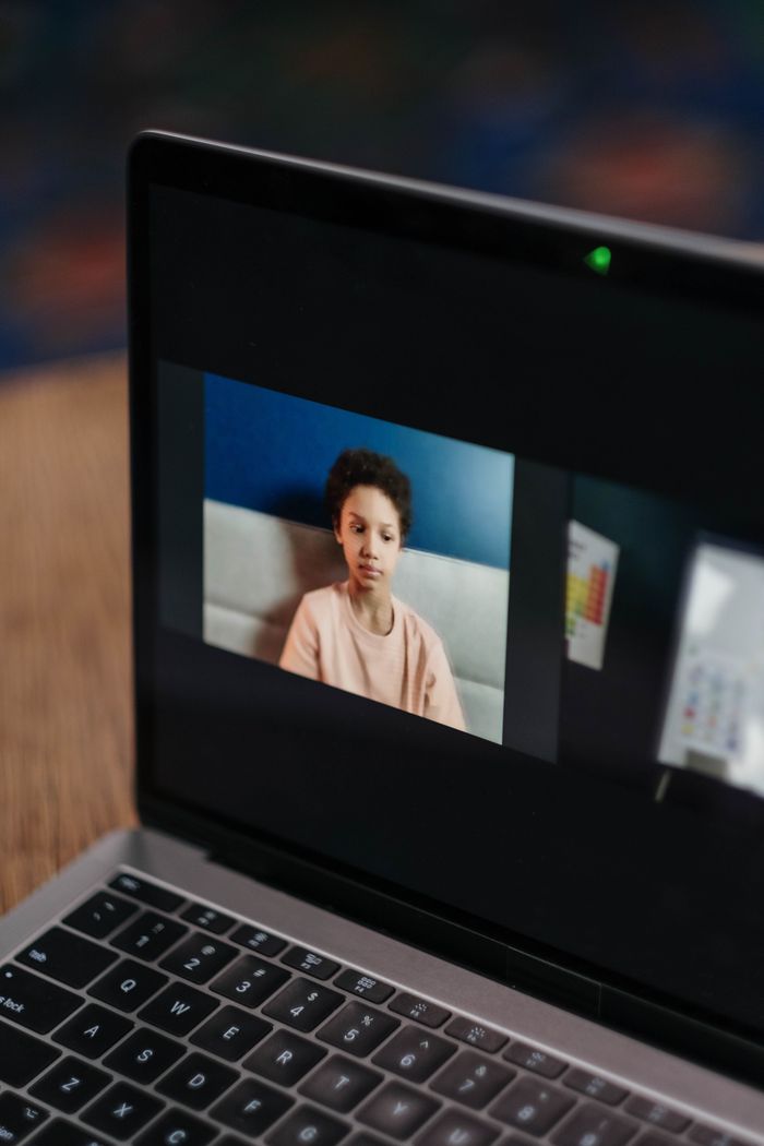 A young African American girl takes part in an online class from home using a laptop.