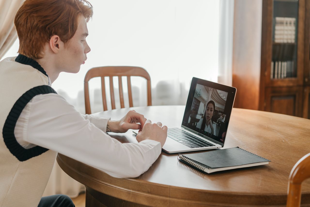 A young man is taking part in a video call on a laptop at home, showing remote communication.