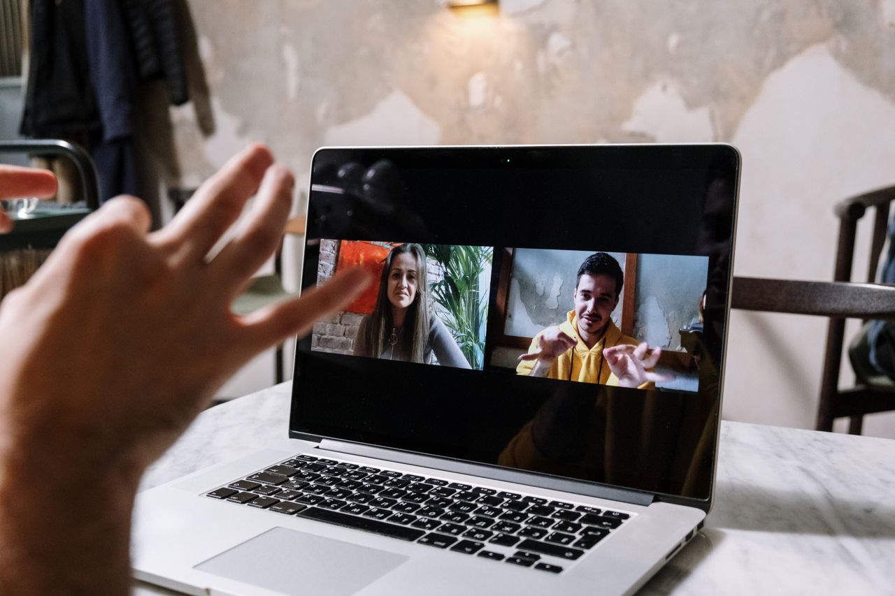 Hands moving during a video call displayed on a laptop screen, illustrating two people in a virtual meeting.